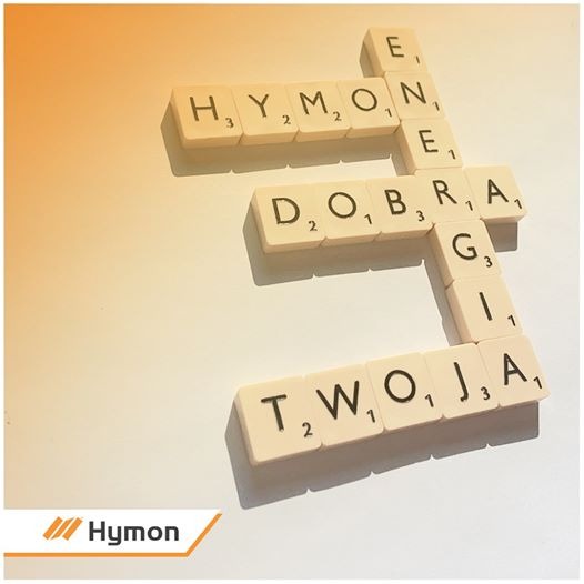 Kreatywna kompozycja z płytek do Scrabble układających się w słowa 'Hymon Energia Dobra Twoja' na jasnym tle z logo firmy Hymon w lewym dolnym rogu.