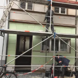 Prace ociepleniowe na elewacji budynku z użyciem rusztowania; widoczni dwaj pracownicy, jeden na górze, drugi na dole, oraz rower zaparkowany obok