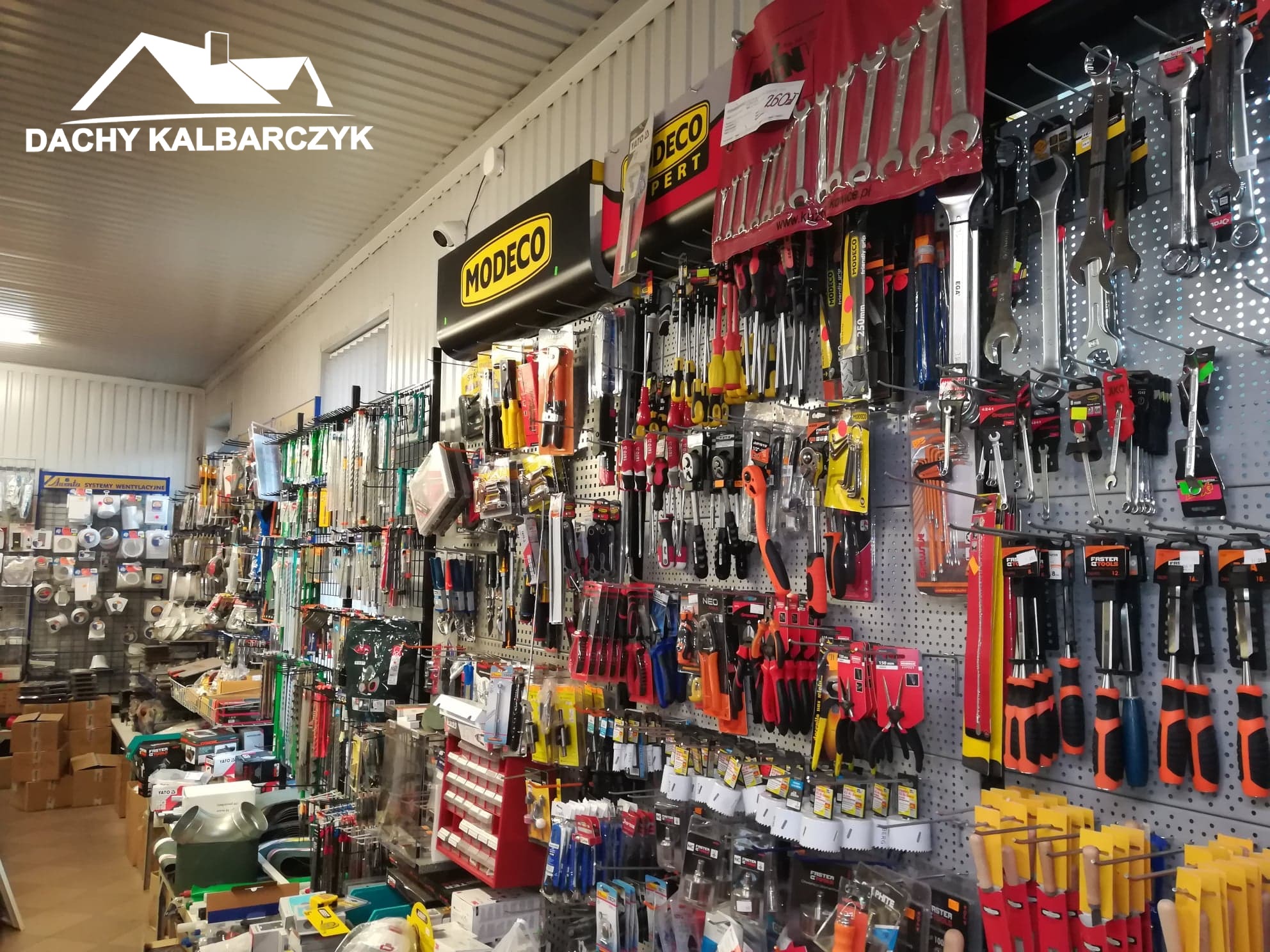 Wnętrze sklepu z narzędziami i akcesoriami budowlanymi, ściany pokryte perforowanymi panelami ekspozycyjnymi, widoczne różnorodne narzędzia ręczne, elektronarzędzia i materiały montażowe...
