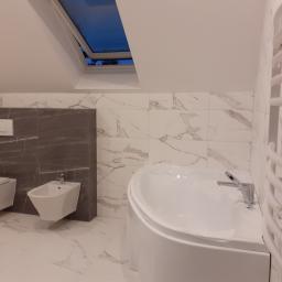 Bud-mar Mariusz Kos usługi ogólnobudowlane. - Wykończona łazienka na poddaszu z oknem dachowym, białą armaturą (toaleta, bidet, wanna) i grzejnikiem drabinkowym, płytki imitujące marmur.