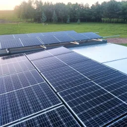 Instalacja paneli słonecznych na dachu budynku z widokiem na zieloną okolicę w tle.