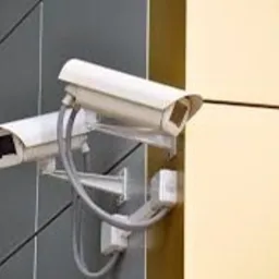 Dwie białe kamery monitoringu zewnętrznego, zamontowane na ścianie budynku, widoczne przewody połączeniowe.