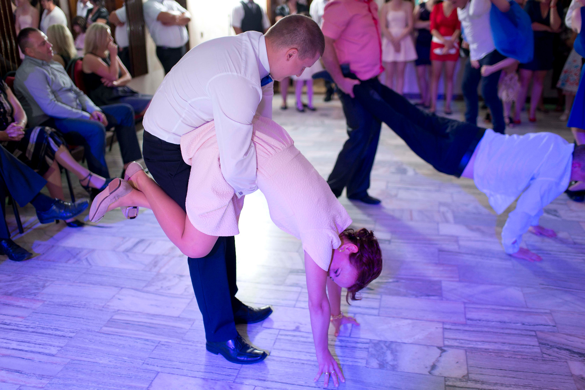 Para podczas weselnej zabawy 'pod mostem' na parkiecie w sali balowej, w tle goście weselni.