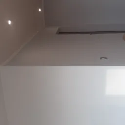 Świeżo pomalowane, jasnoszare ściany z zamontowanym drewnianym blatem składanym i wpuszczanymi punktami świetlnymi w suficie.