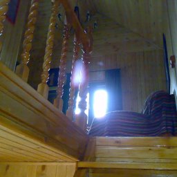 Krakusserwis - Wnętrze drewnianego domu z widocznymi schodami z kręconymi balustradami, oświetlonymi przez jasne światło wpadające przez okno.