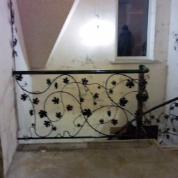 Krakusserwis - Kuta, metalowa balustrada schodowa z motywem winorośli w surowym wnętrzu, widoczne ślady po pracach wykończeniowych na ścianach i podłodze.