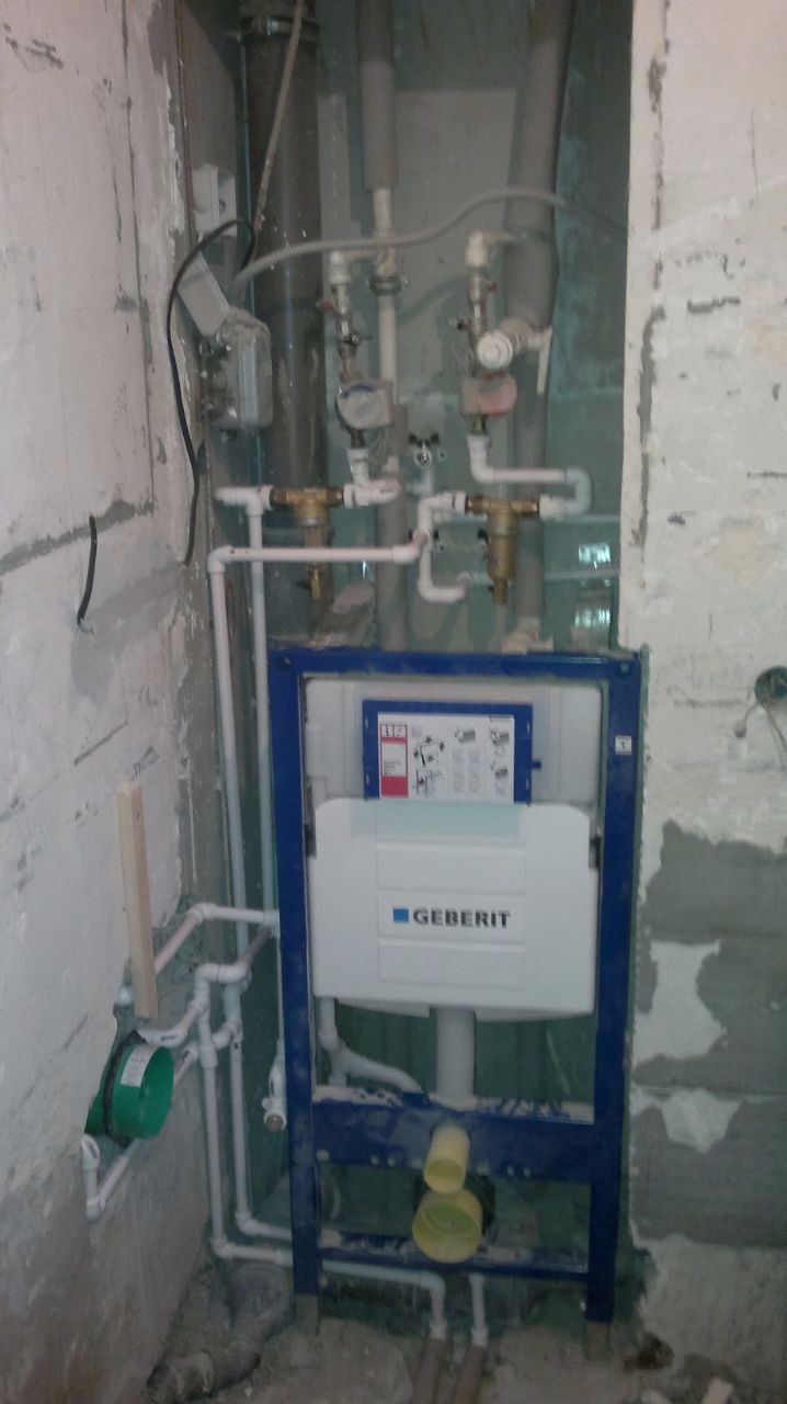 Stelaż podtynkowy Geberit zamontowany w surowym wnętrzu łazienki, widoczne rury instalacyjne i fragmenty nieotynkowanej ściany.