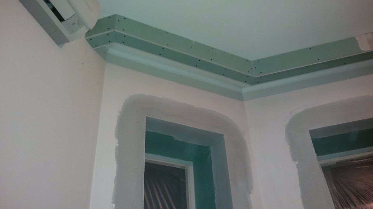 Montaż płyty karton gips na suficie z widocznymi śrubami mocującymi, obok klimatyzator, ściany przygotowane do malowania z obrobionymi otworami drzwiowymi.