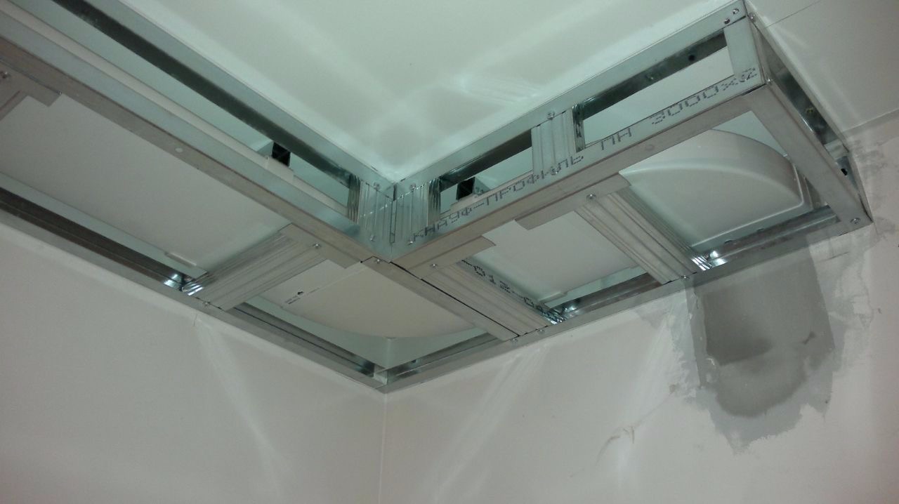 Montaż metalowej konstrukcji sufitu podwieszanego z widocznymi profilami i częściowo zamontowanymi panelami, widoczne ślady szpachlowania na ścianie.