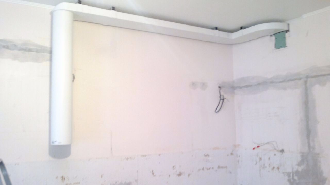 Biały kanał wentylacyjny z pionową rurą na ścianie w trakcie remontu, widoczne ślady po szpachlowaniu i wystające przewody elektryczne.