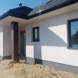 Nowoczesny dom jednorodzinny w Tomaszowie Mazowieckim po tynkowaniu i ociepleniu elewacji, z widocznym fragmentem elewacji pokrytej białą strukturą, stolarką okienną w kolorze antracytowym...