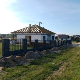 Fenstahab - Budowa domu jednorodzinnego w trakcie realizacji: surowy stan otwarty z więźbą dachową, ogrodzenie panelowe z podmurówką, pryzmy piasku wzdłuż ogrodzenia.