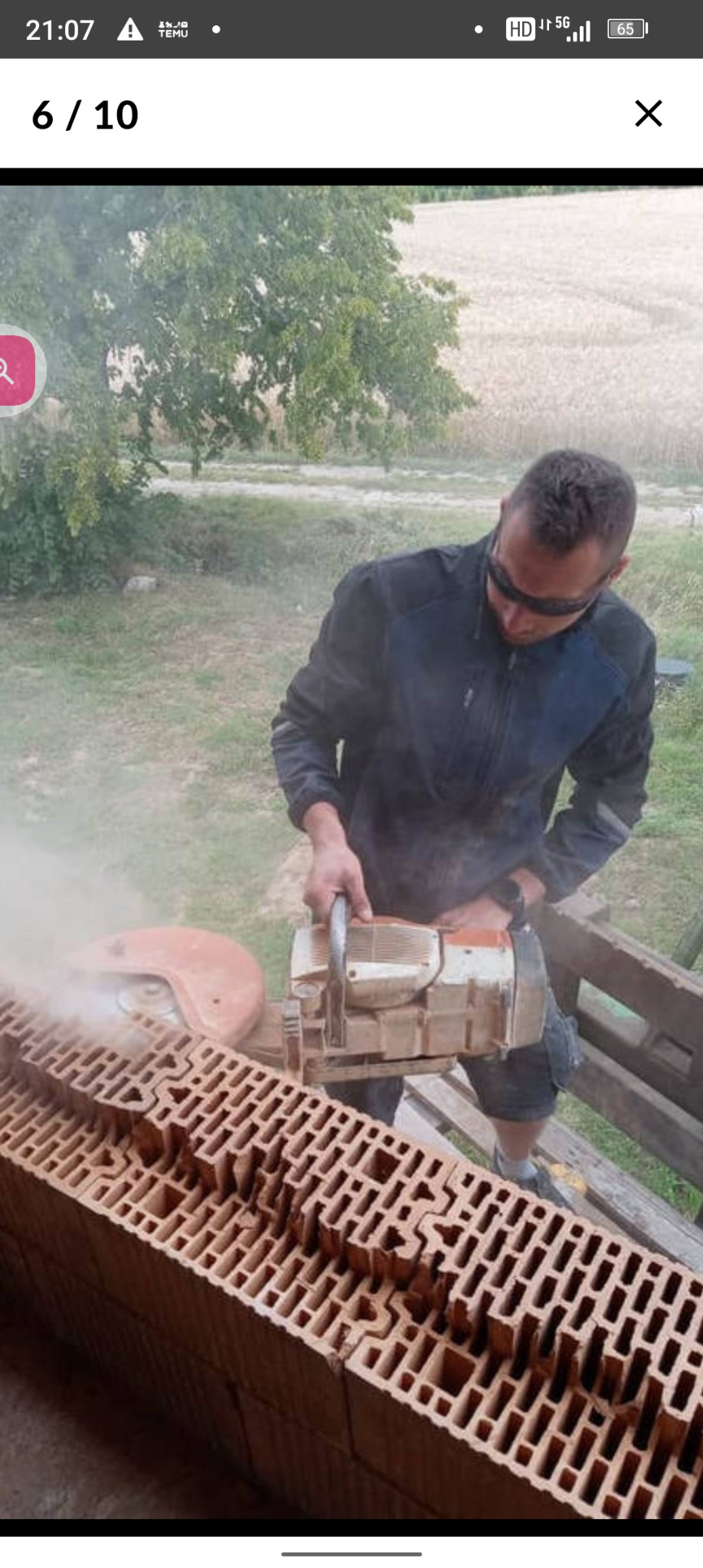 Pracownik w okularach ochronnych przecina bloczki ceramiczne piłą spalinową na zewnątrz, unoszący się pył.