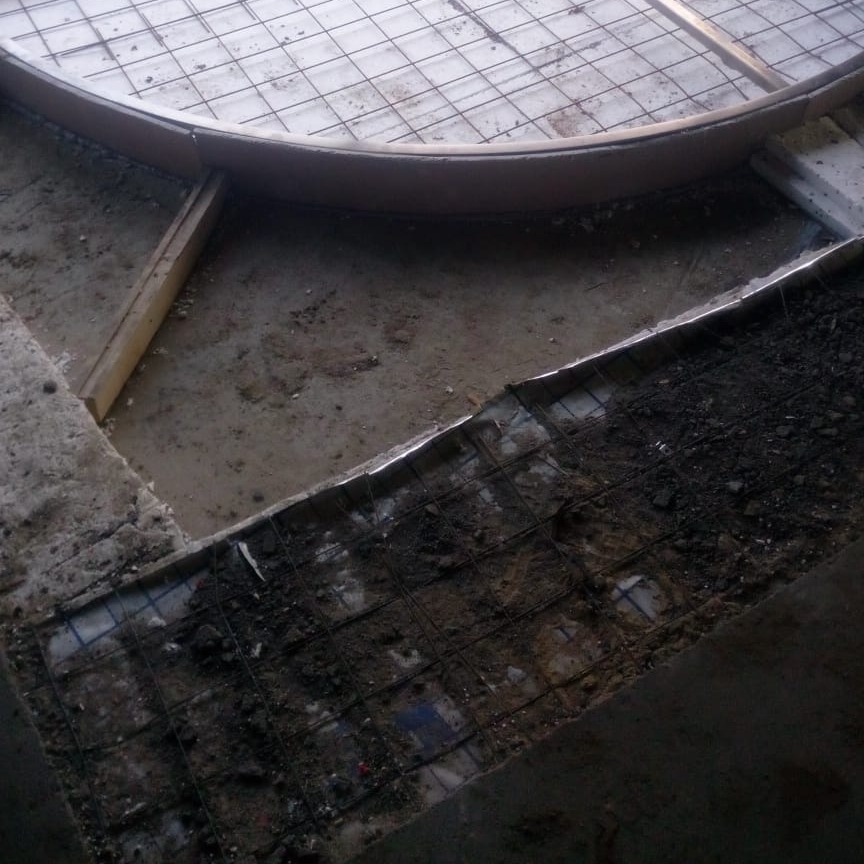 Przygotowanie podłoża pod wylewkę z siatką zbrojeniową i drewnianym szalunkiem o zaokrąglonym kształcie, widoczne warstwy gruzu i ziemi.