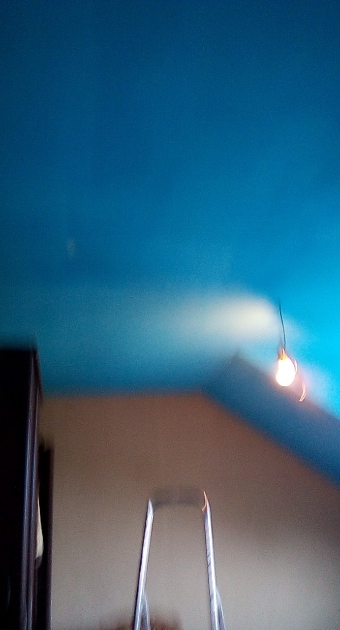 Niedoskonałe ujęcie niebieskiego sufitu z wiszącą żarówką i fragmentem drabiny malarskiej, widoczny bok szafy.