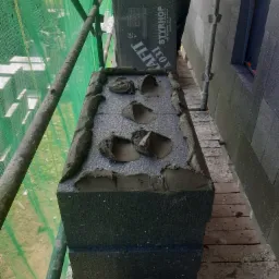 Montaż termoizolacyjnych płyt styropianowych z zaprawą klejową na elewacji w Dąbrówce, widoczne rusztowanie i pracownik w tle.