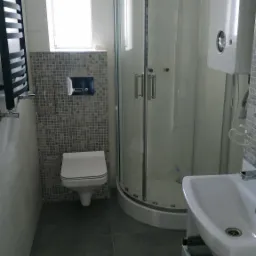 Nowoczesna łazienka z kabiną prysznicową narożną, wiszącą toaletą z mozaiką na ścianie, umywalką na postumencie i grzejnikiem drabinkowym