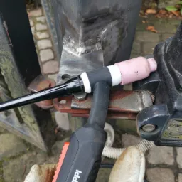 Spoina na metalowej konstrukcji bramy w Gdańsku, wykonana metodą TIG, widoczny uchwyt spawalniczy Kemppi i rękawica ochronna.