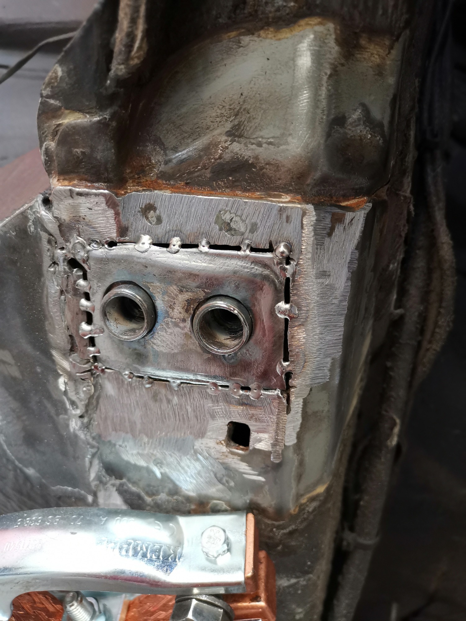 Fragment karoserii po naprawie blacharskiej z widocznymi śladami spawania i nowo wspawanymi rurkami, uchwyt spawalniczy w dolnej części kadru.