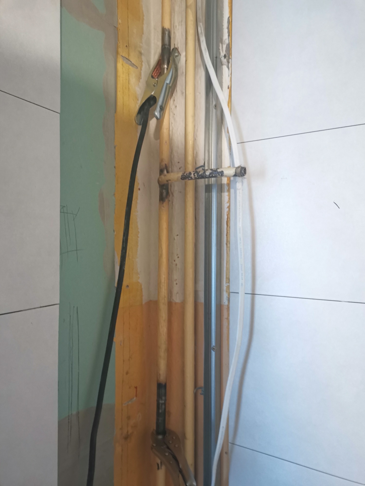 Spawanie rur miedzianych w ścianie, widoczne elektrody, zacisk i narzędzia ślusarskie.