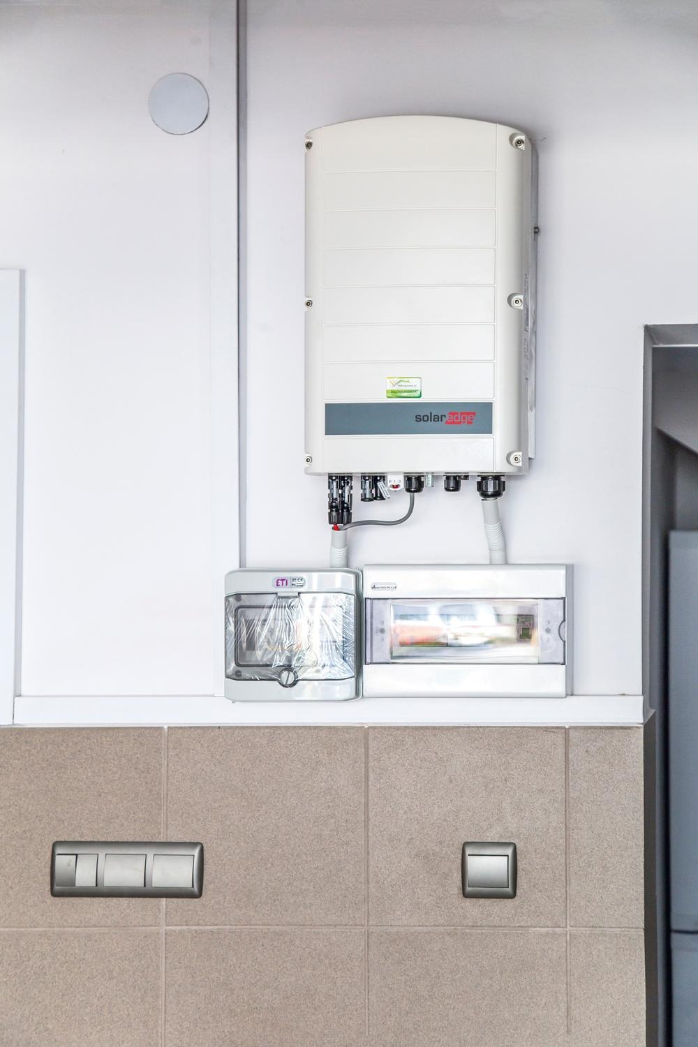 Zamontowany inwerter SolarEdge wraz z zabezpieczeniami elektrycznymi i rozdzielnicą, widoczne na tle ściany wyłożonej kafelkami.