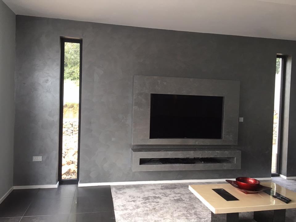 Szara ściana z efektem dekoracyjnym w nowoczesnym salonie, z wnęką na telewizor i wąskim oknem z widokiem na zieleń.