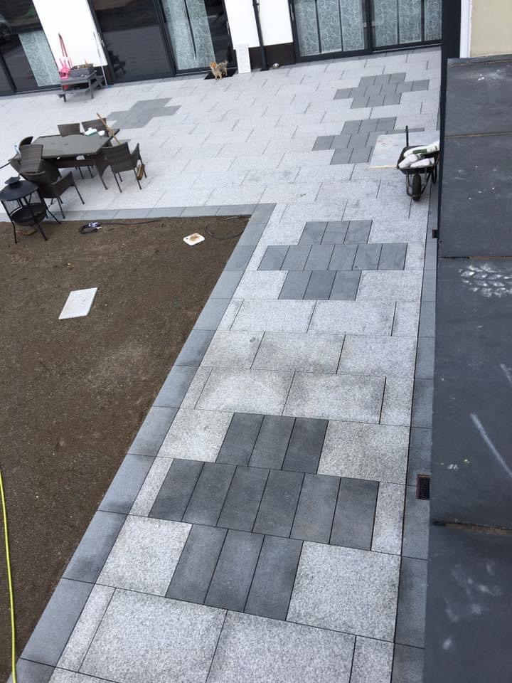 Nowoczesny taras z szarej kostki brukowej ułożonej w geometryczny wzór krzyży, widok z góry, z elementami trawnika i meblami ogrodowymi.