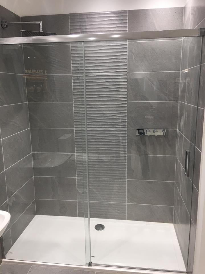 Szara kabina prysznicowa z przesuwnymi drzwiami i panelami dekoracyjnymi o falistej strukturze, zamontowana w wykończonej łazience.