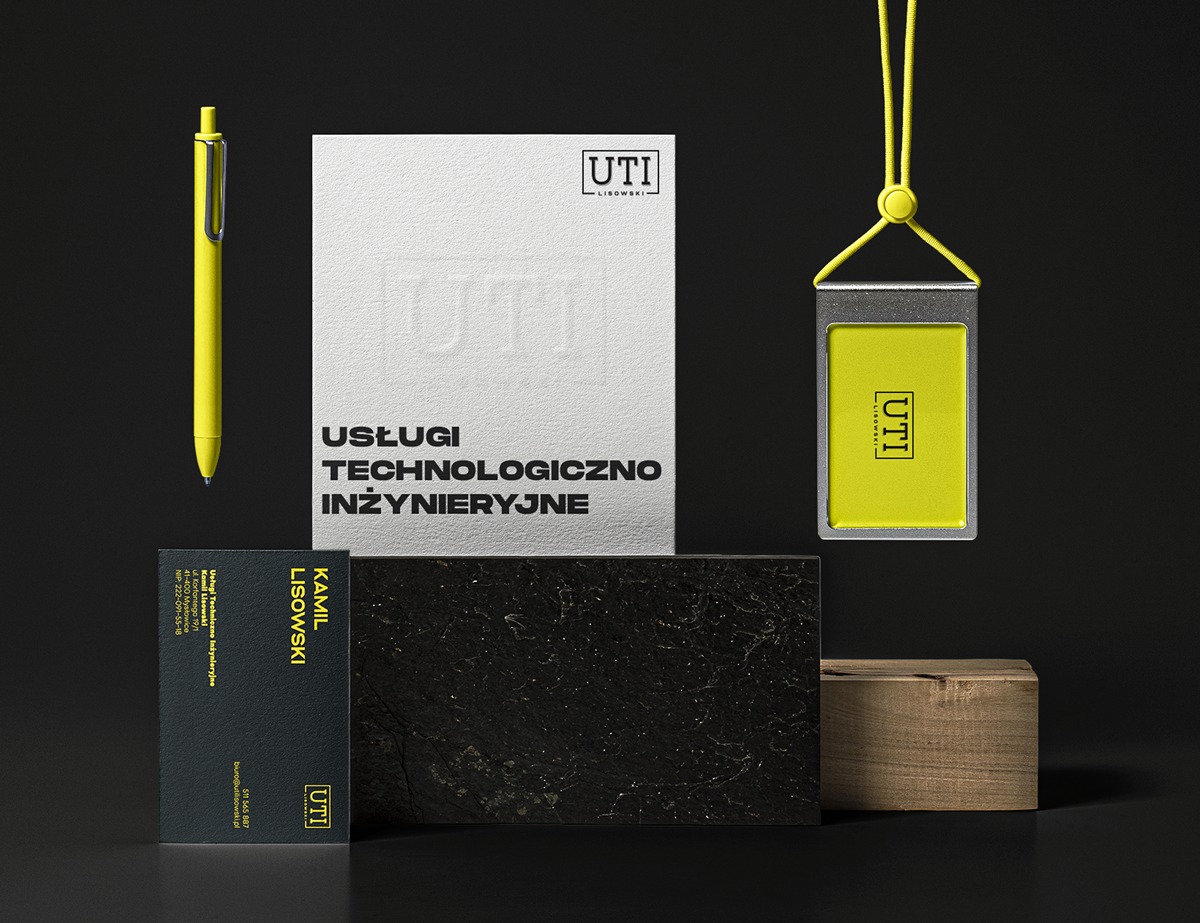 Zestaw materiałów firmowych w odcieniach czerni, bieli i żółci: wizytówka z danymi kontaktowymi, identyfikator na smyczy, notatnik z tłoczonym logo i długopis, całość na ciemnym tle z elementami...