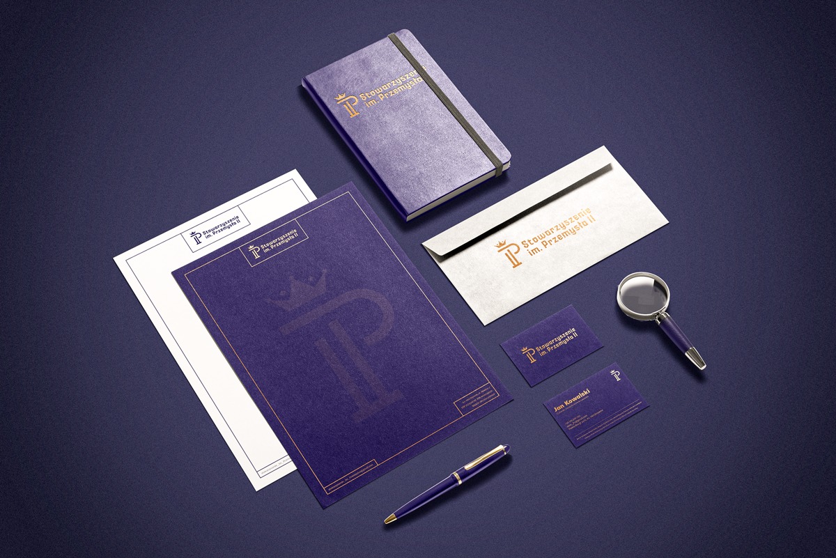 Komplet materiałów firmowych w odcieniach fioletu i złota: notes, koperta, wizytówki, papier firmowy i lupa, ułożone na ciemnym tle.