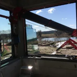 Montaż okna za pomocą przyssawki i dźwigu w surowym stanie budynku, widok na rzekę i drzewa