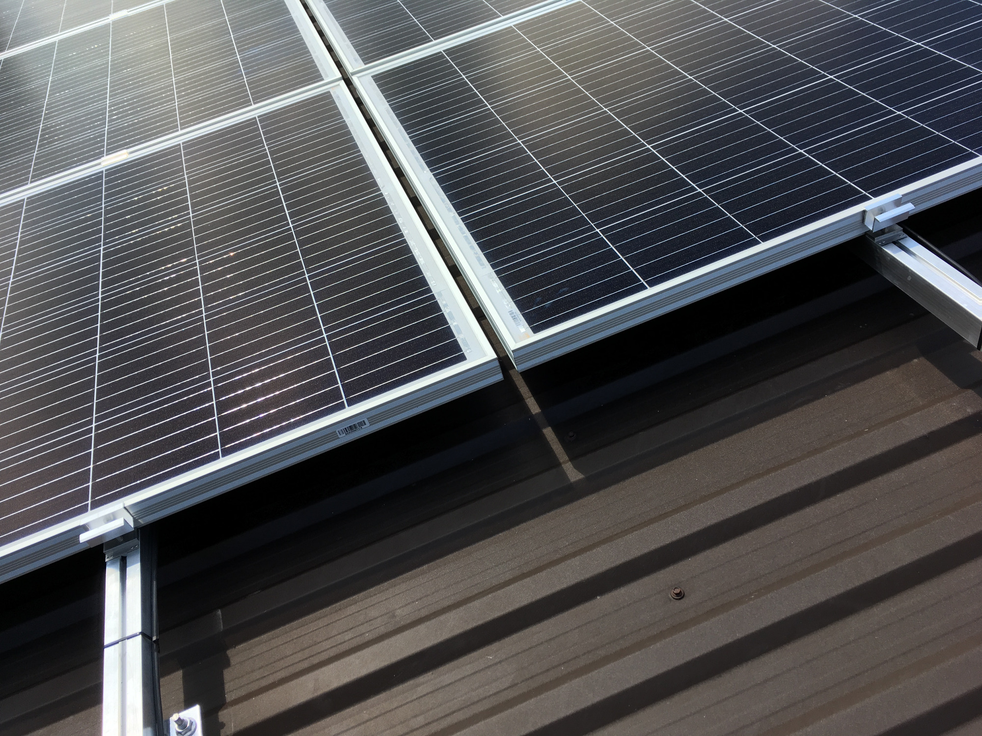 Panele słoneczne zamontowane na brązowym dachu z blachy trapezowej, widoczne elementy montażowe.