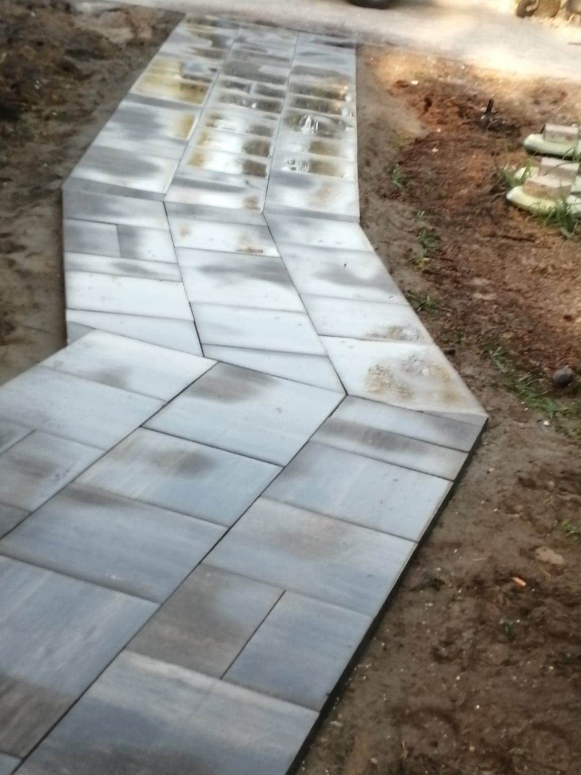 Ścieżka z szarych, prostokątnych płyt brukowych, ułożona na ziemi, widoczna z góry, z lekkim ukosem.