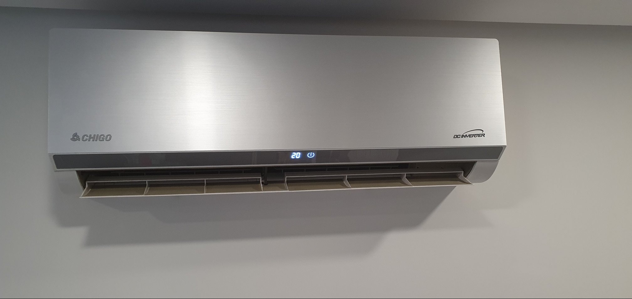 Szara klimatyzacja Chigo typu split, zamontowana na jasnej ścianie, wyświetla temperaturę 20 stopni Celsjusza.