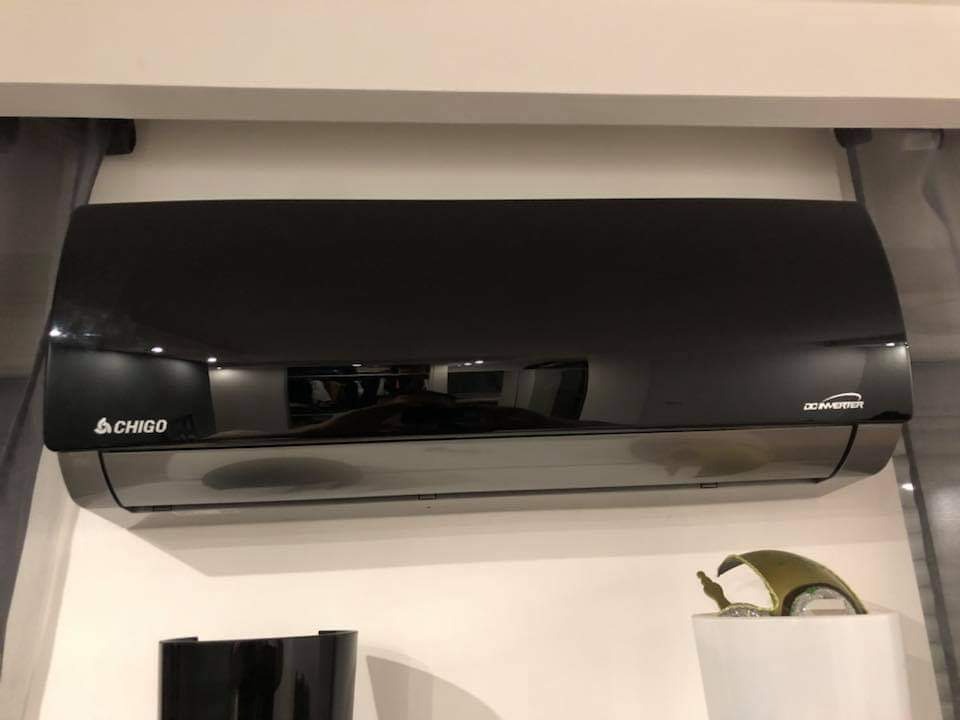 Czarna, błyszcząca klimatyzacja marki Chigo, zamontowana na białej ścianie w pomieszczeniu z elementami dekoracyjnymi.