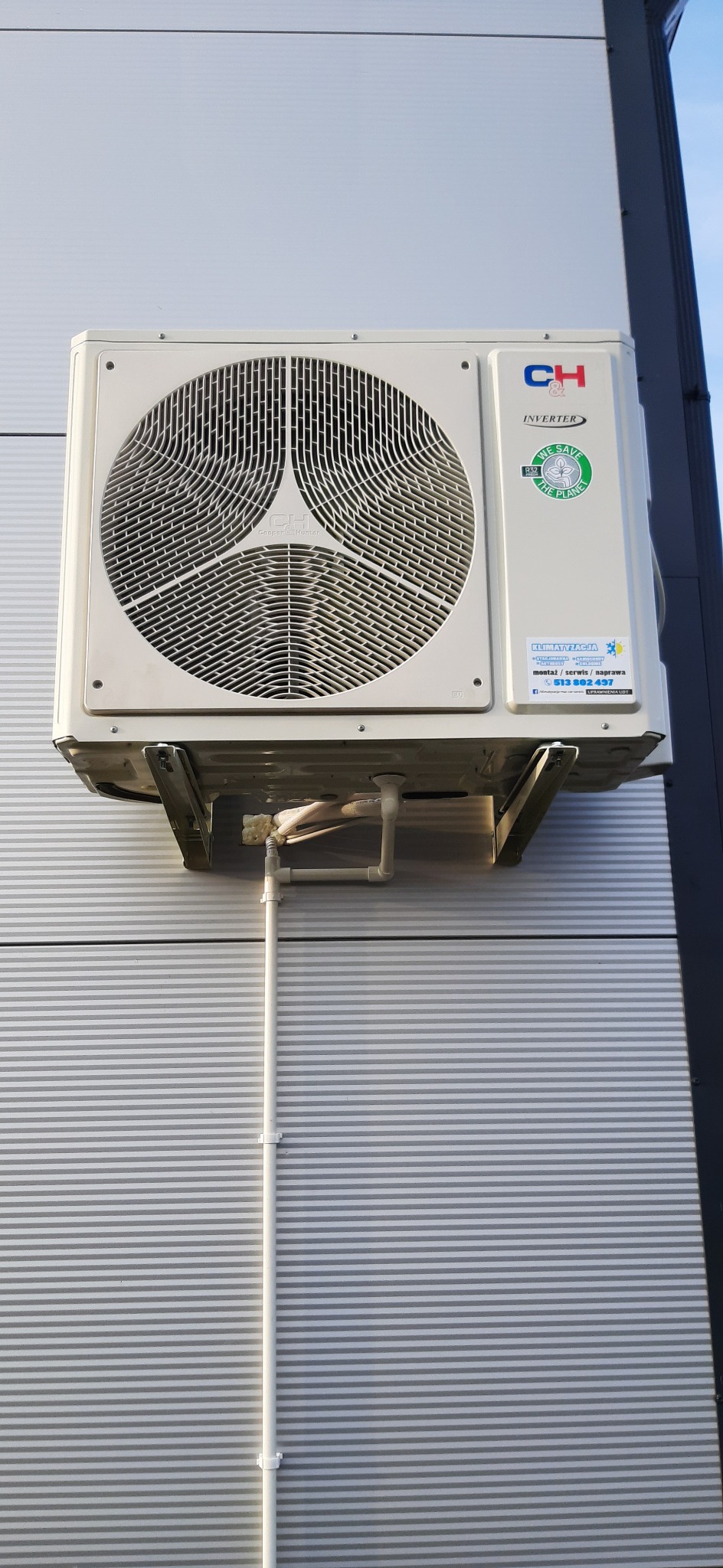 Zewnętrzna jednostka klimatyzacji marki CH Inverter, zamontowana na metalowej elewacji budynku w Rzeszowie, z widocznymi rurami odprowadzającymi skropliny i naklejką informującą o montażu, serwisie...