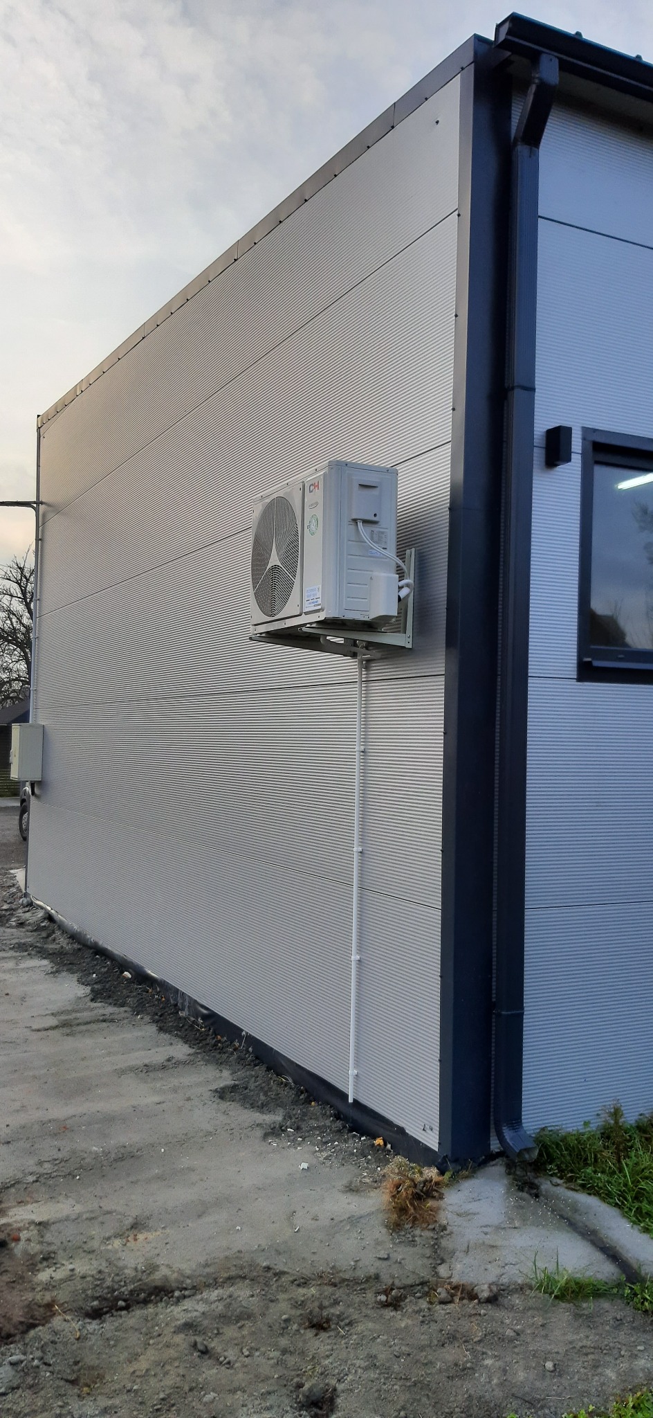 Zewnętrzna jednostka klimatyzacji marki CH zamontowana na metalowej ścianie hali przemysłowej z widocznymi rurami odprowadzającymi skropliny.