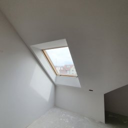 360 Marketing Kamil Modzelewski - Pomalowane na biało poddasze z oknem dachowym; widoczne fragmenty zabudowy i nie do końca wyschnięta podłoga.