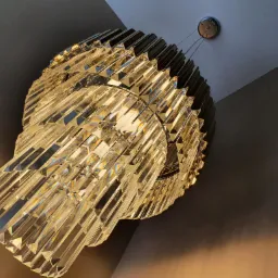 Dwupoziomowy, kryształowy żyrandol z metalowym wykończeniem, widziany z dołu, z widocznymi załamaniami światła na kryształach i fragmentem sufitu.