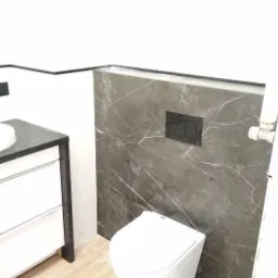 Ścianka z szarego marmuru z czarnym przyciskiem spłukującym nad podwieszaną białą toaletą, obok umywalka z szafką, wykończona czarną listwą, na podłodze płytki imitujące drewno.