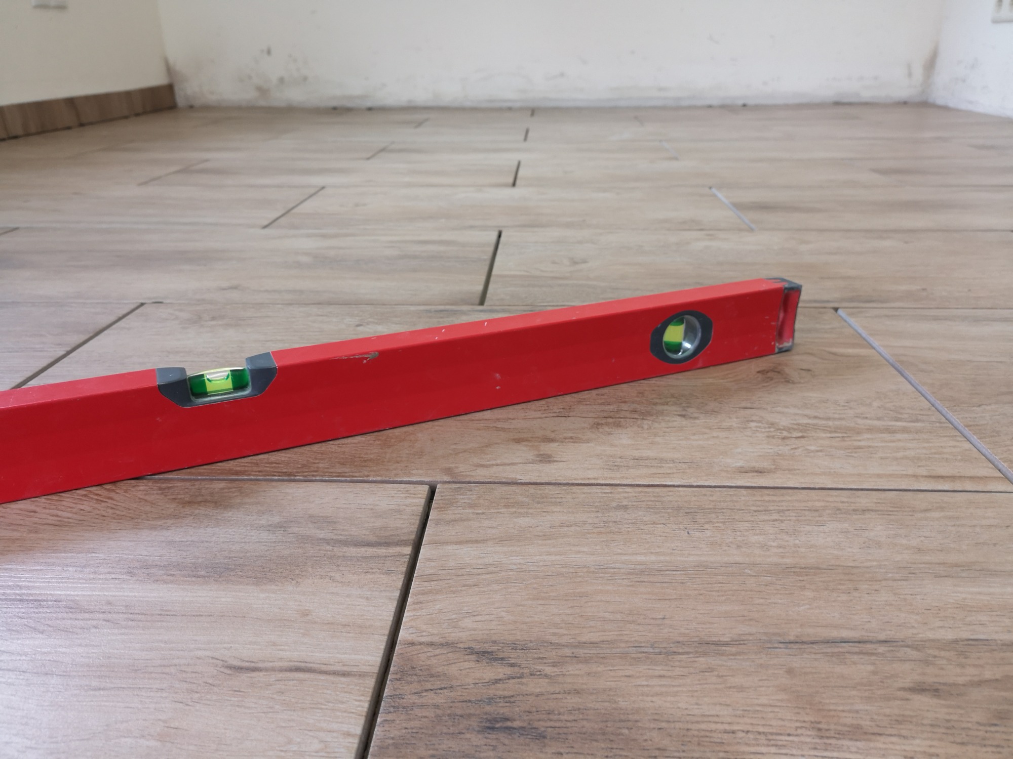 Położone płytki podłogowe imitujące drewno, z widoczną czerwoną poziomicą wskazującą na prawidłowy poziom; widoczne fugi i fragment ściany w tle.