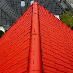 Intensywnie czerwony dach z dachówki ceramicznej, widok z góry, sąsiedni dach w kolorze grafitowym, w tle biały samochód dostawczy.