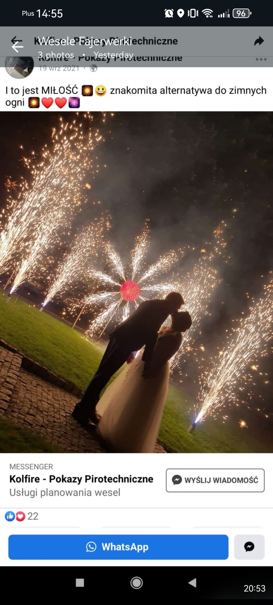 Para młoda całuje się na tle efektownego pokazu fajerwerków podczas wesela. W tle zielony trawnik i ciemne niebo rozświetlone sztucznymi ogniami.