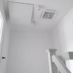 Białe wnętrze z zamontowanym klimatyzatorem kasetonowym i klapą rewizyjną w suficie, widok z dołu.