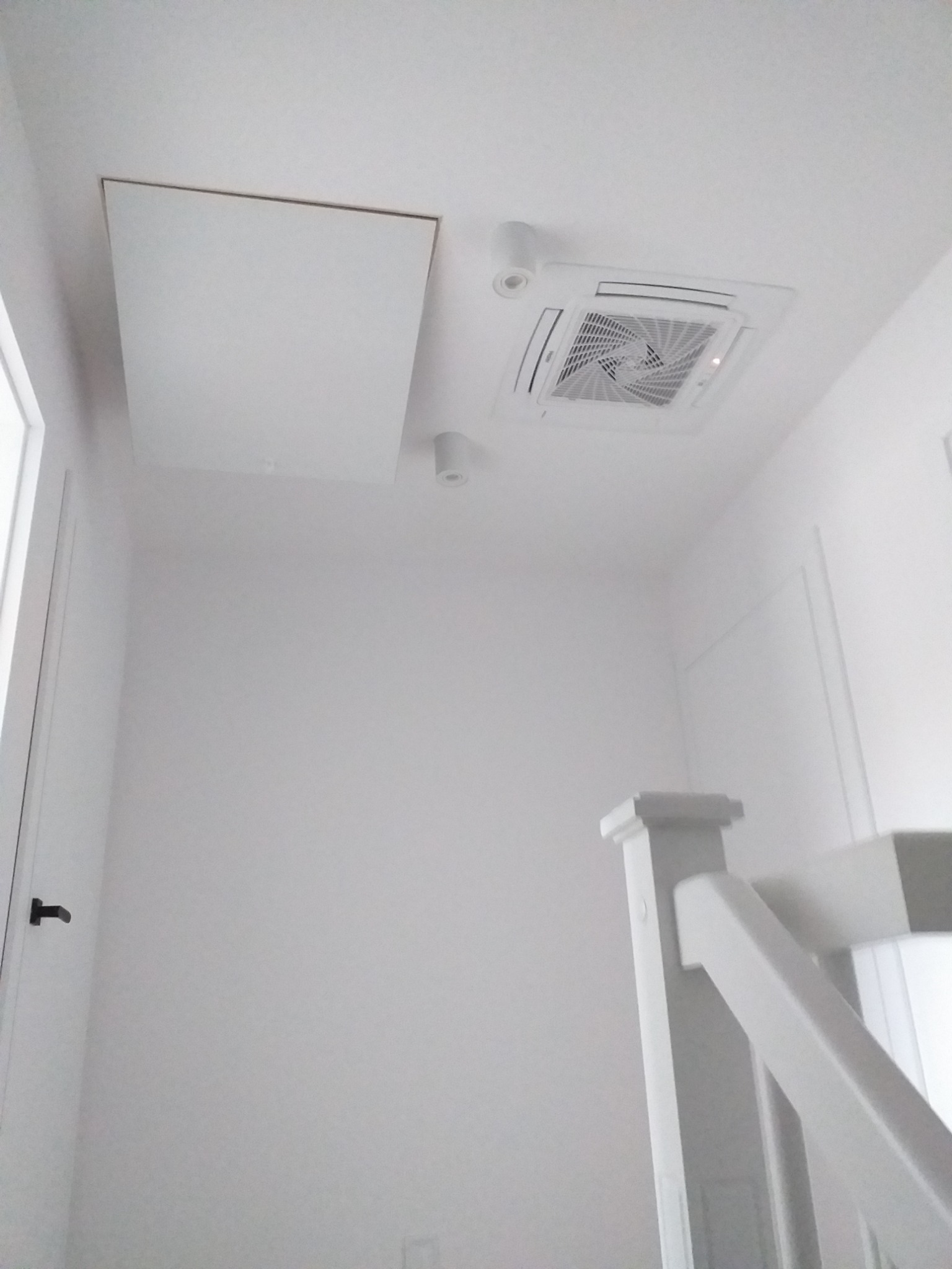 Białe wnętrze z zamontowanym klimatyzatorem kasetonowym i klapą rewizyjną w suficie, widok z dołu.