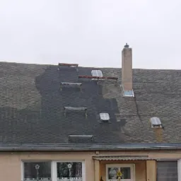 Dach pokryty szarą dachówką łuskową z widocznymi śladami po czyszczeniu, okna dachowe, komin i zabezpieczenia przeciwśniegowe. Część dachu jest wyraźnie jaśniejsza po umyciu.