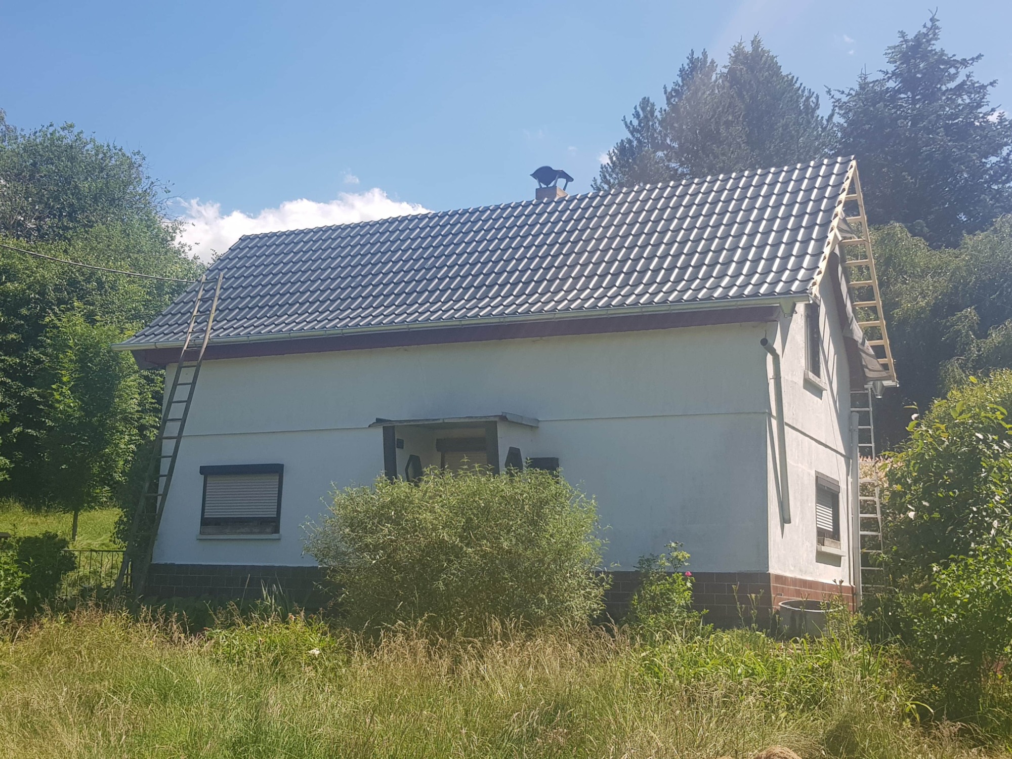 Dom jednorodzinny z nowym, szarym dachem z dachówki ceramicznej, z widoczną konstrukcją szczytową i dwoma przystawionymi drewnianymi drabinami.