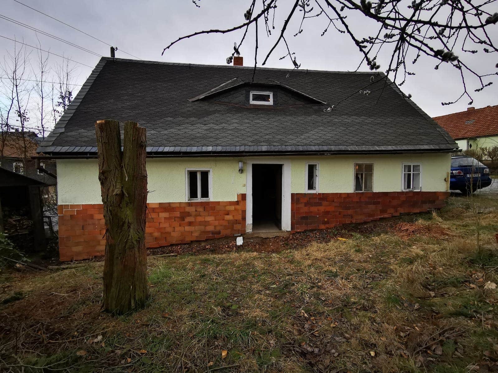 Dom z ciemnoszarym dachem z dachówki łuskowej i ceglaną podmurówką, widok z zewnątrz w pochmurny dzień.