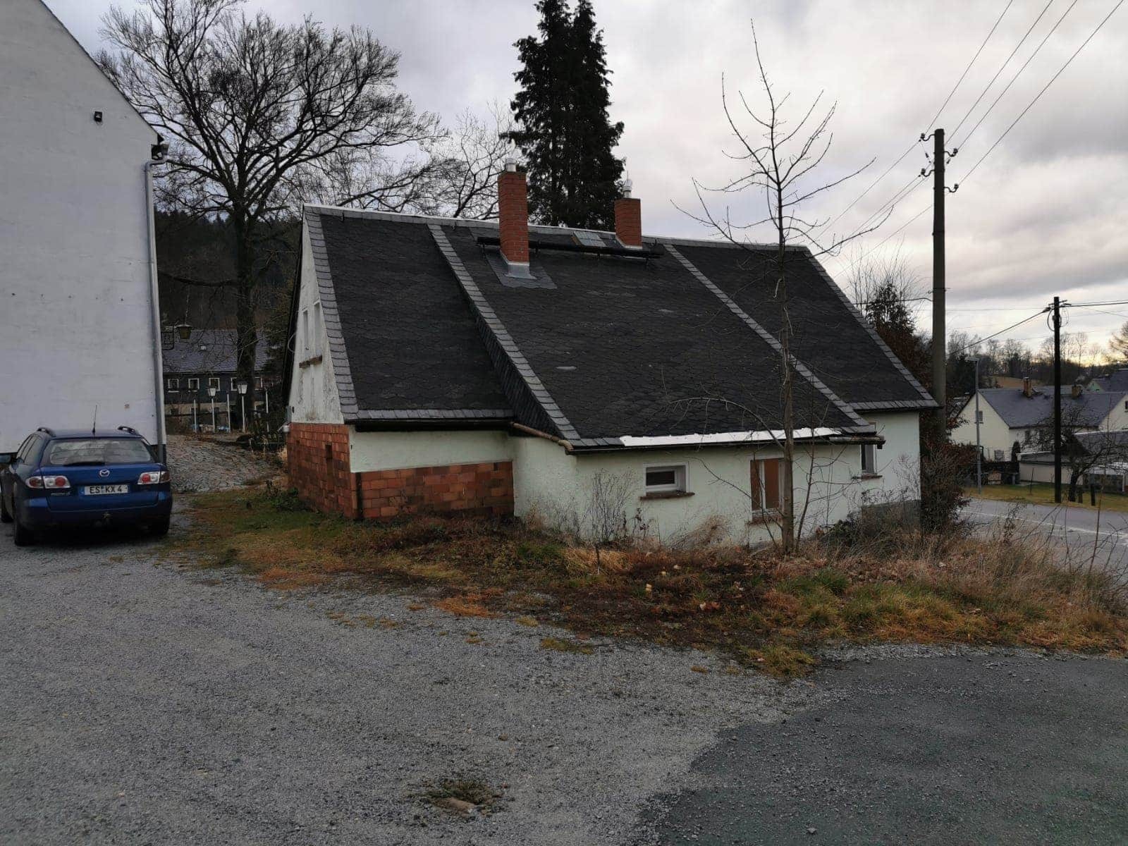 Dom z ciemnym, łupkowym pokryciem dachowym i dwoma kominami z cegły, widoczny z poziomu gruntu, z samochodem zaparkowanym obok.