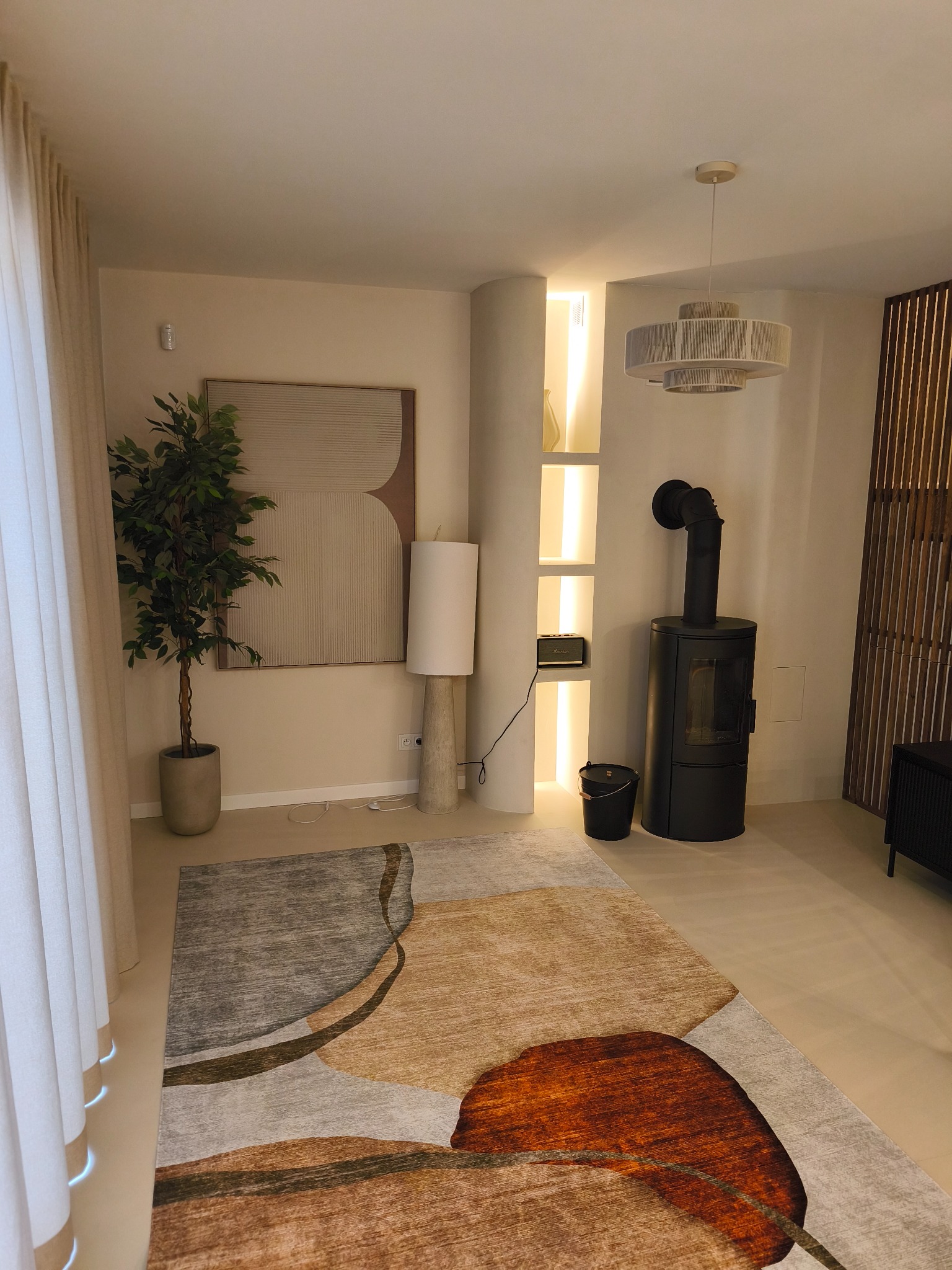 Nowoczesny salon z kominkiem, lampą podłogową i designerskim dywanem w odcieniach brązu i szarości. Minimalistyczne wnętrze z rośliną doniczkową i abstrakcyjnym obrazem.